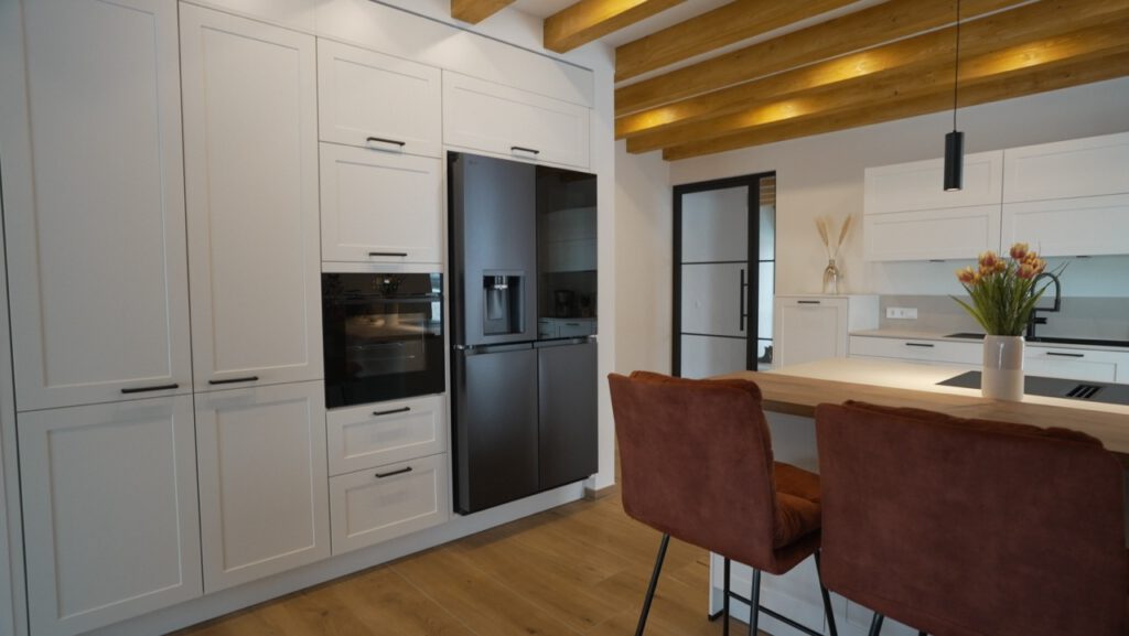 Moderne Küche mit weißen Schränken, dunklem Kühlschrank, Holzarbeitsplatte und rötlichen Barhockern.