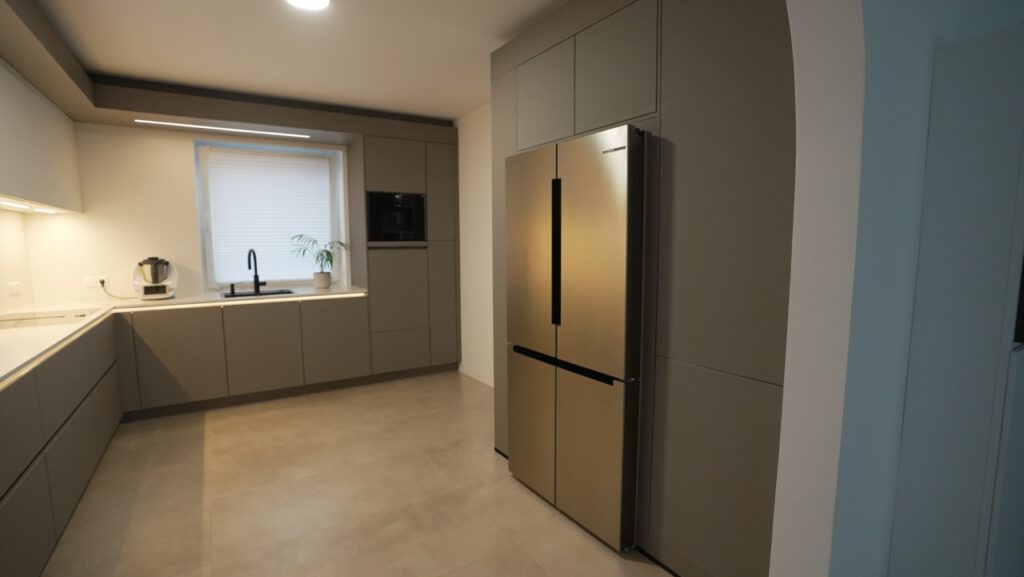 Moderne, aufgeräumte Küche mit Edelstahlkühlschrank, Küchenzeile, Mixer und Topfpflanze am Fenster.