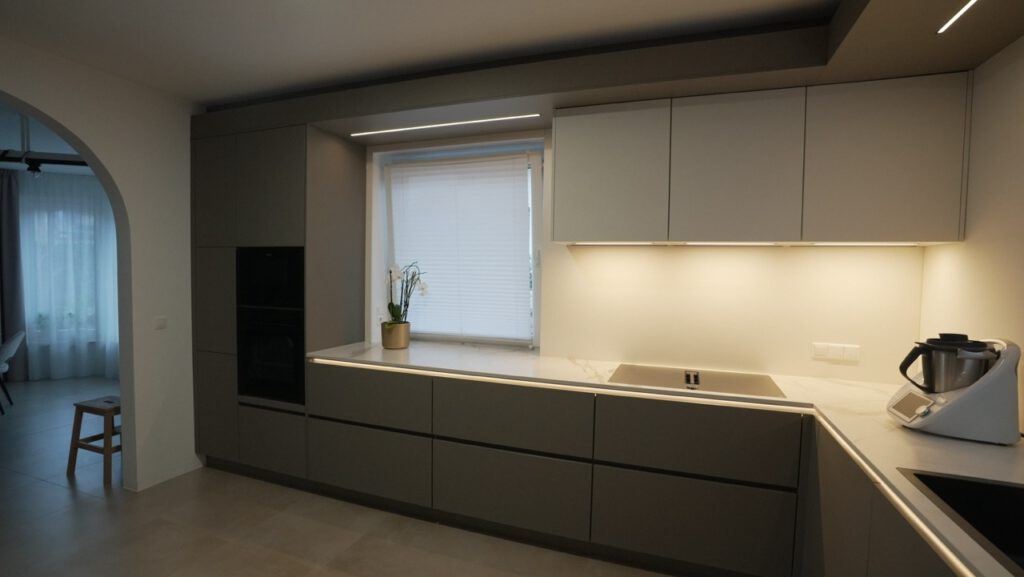 Moderne, minimalistische Küche mit grauen Fronten, natürlichem Licht und einer Pflanze auf der Arbeitsplatte.