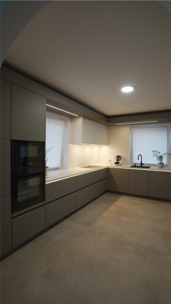 Moderne, minimalistische Küche mit grauen Schränken, natürlichem Licht und zwei kleinen Pflanzen.