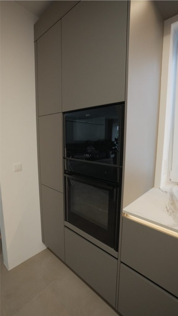 Moderne graue Einbauküche mit matten Fronten, glänzend schwarzen Geräten und heller Arbeitsplatte.