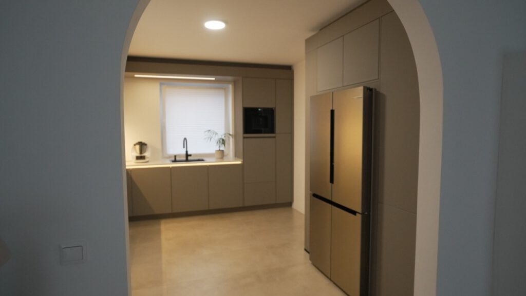 Moderne Küche mit beigen Schränken, goldenem Kühlschrank und Pflanze auf der Fensterbank.