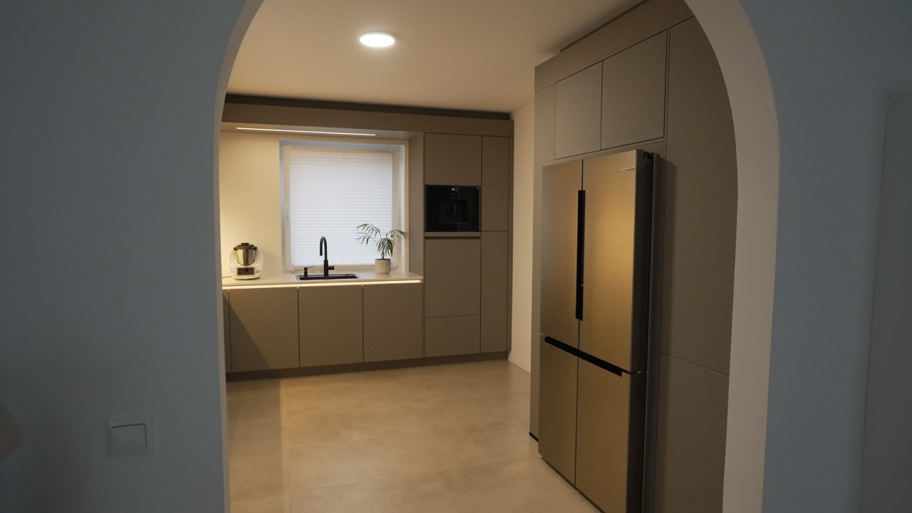 Moderne, minimalistische Küche in Beige und Grau mit Kühlschrank, Küchenzeile und Topfpflanze.