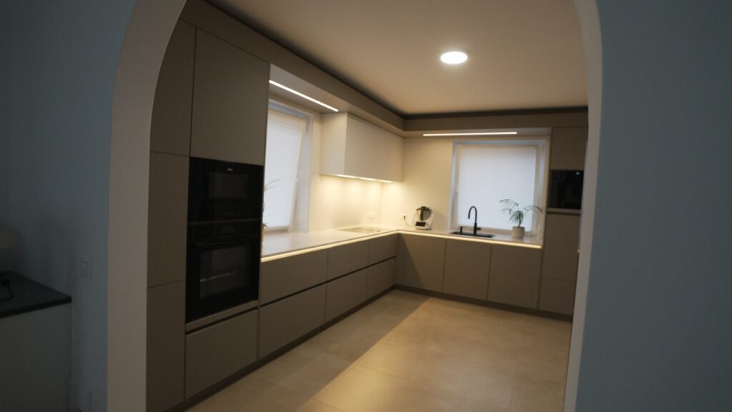Moderne, aufgeräumte Küche mit neutralen Tönen, integriertem Backofen und warmer Beleuchtung.