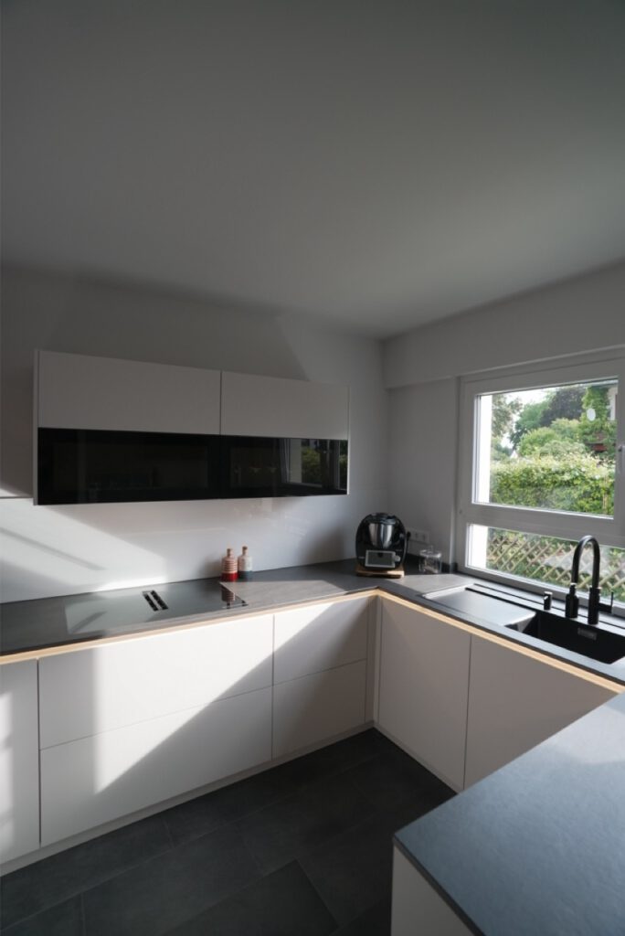 Moderne, minimalistische Küche in Weiß und Schwarz mit Ceran-Kochfeld, schwarzem Waschbecken und Gewürzbehältern.