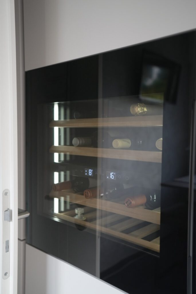 Ein Weinkühlschrank mit Glastür zeigt horizontal gelagerte Weinflaschen auf Holzregalen.