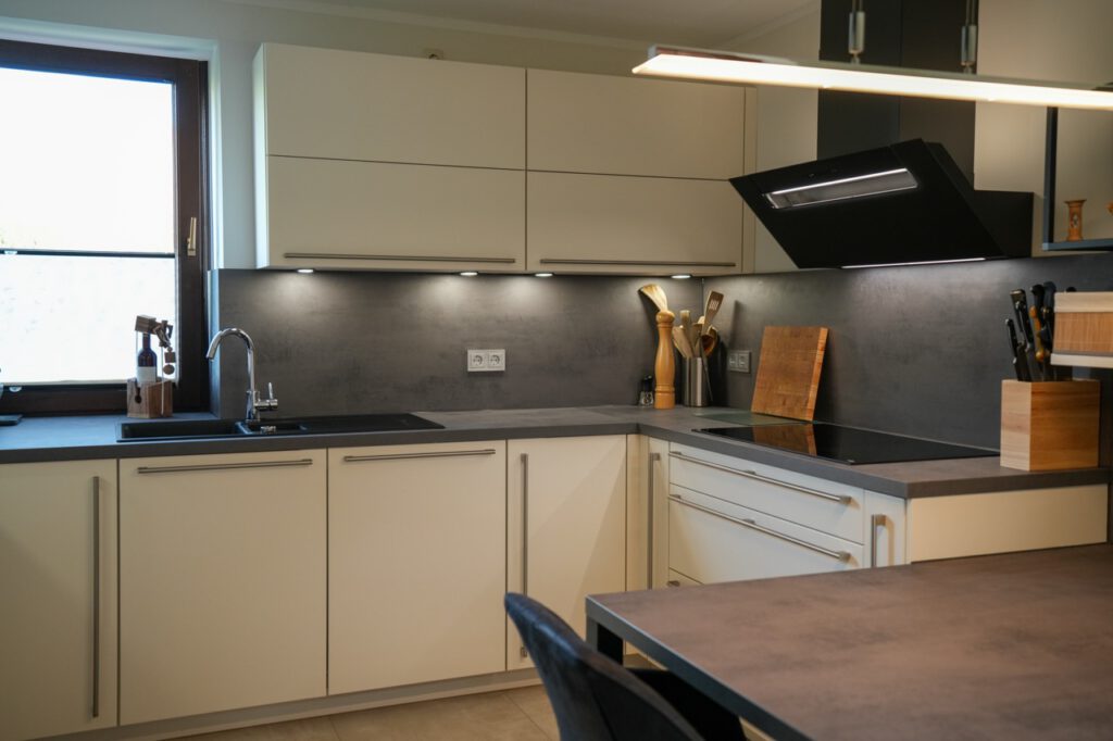 Moderne Küche mit cremefarbenen Schränken, grauer Arbeitsplatte, Edelstahlspüle und Kochfeld.