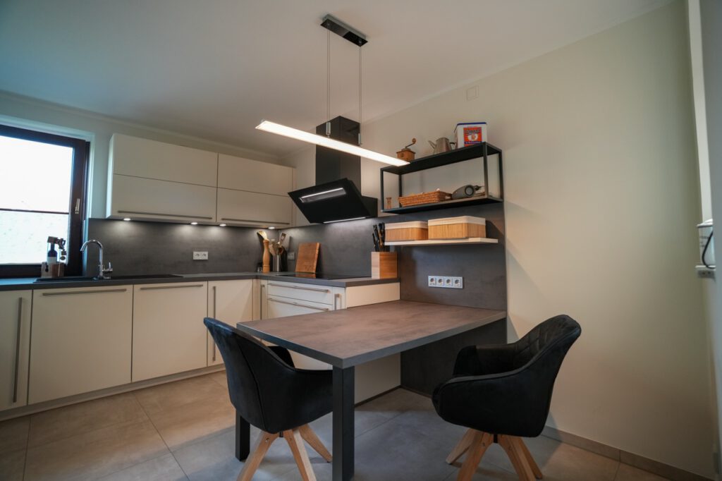 Moderne, minimalistische Küche mit cremefarbenen Schränken, Esstisch und schwarzen Stühlen.