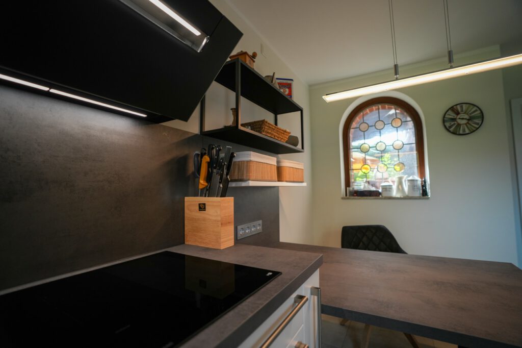 Moderne Küche mit dunkler Arbeitsplatte, Messerblock, buntem Glasfenster und eleganter Beleuchtung.
