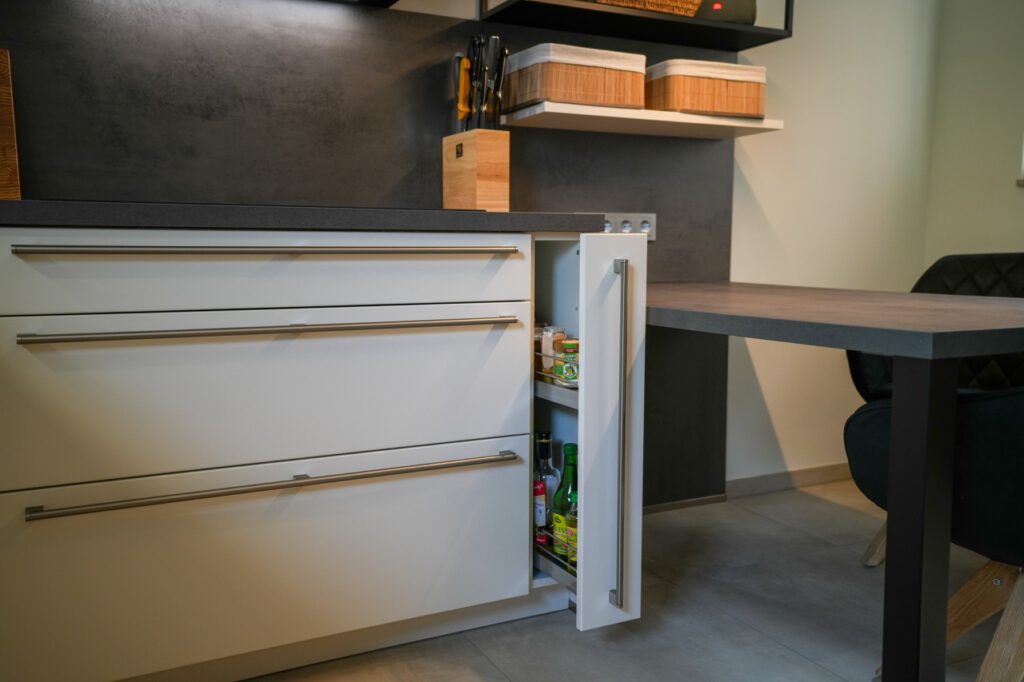 Moderne, aufgeräumte Küche mit weißen Schränken, dunkler Arbeitsplatte und gewebten Aufbewahrungskörben.