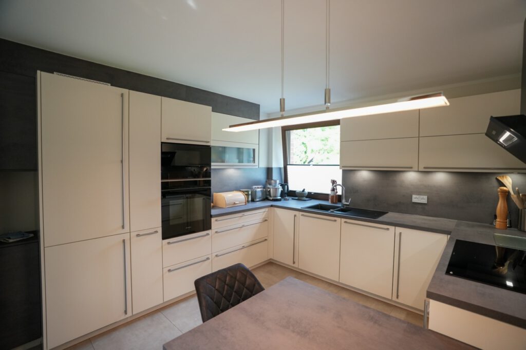 Moderne Küche mit hellen Schränken, dunklen Arbeitsflächen und eleganten Geräten in minimalistischem Design.