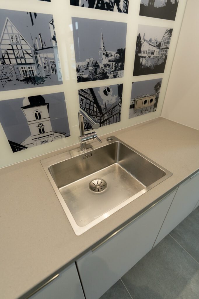 Moderne Küchenspüle aus Edelstahl, helle Arbeitsplatte, architektonische Bilder an der Wand.