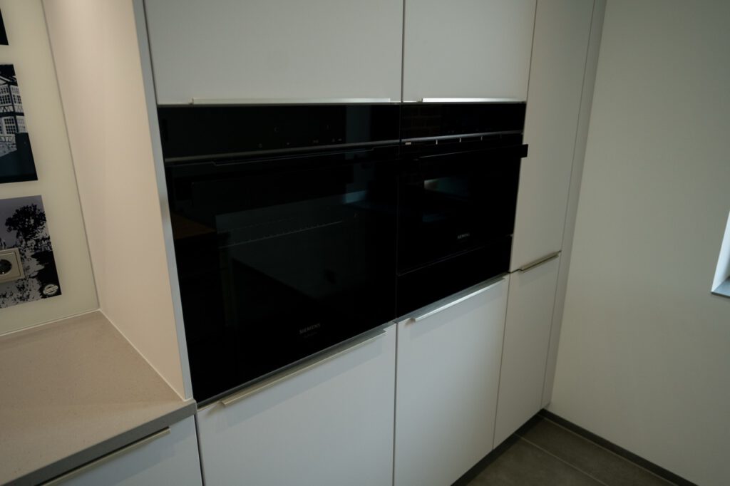 Moderne Küche mit schwarzen Einbaugeräten, weißen Schränken und heller Arbeitsplatte. Minimalistisches Design.