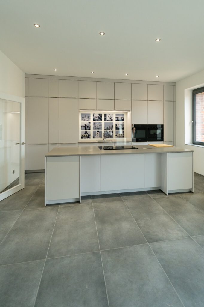 Moderne, minimalistische Küche mit grauer Insel, weißen Schränken und beleuchteten Schwarz-Weiß-Fotos.