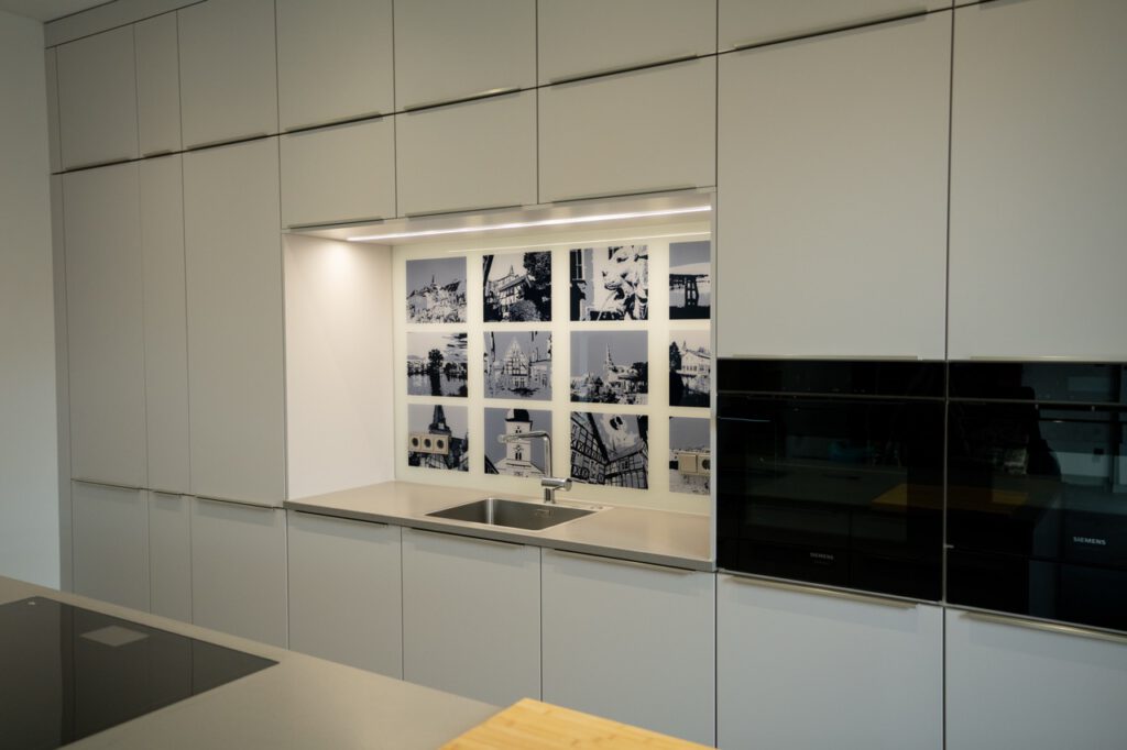 Moderne, minimalistische Küche in Grau und Weiß mit Einbauschränken, Spüle und Schwarz-Weiß-Fotografien.