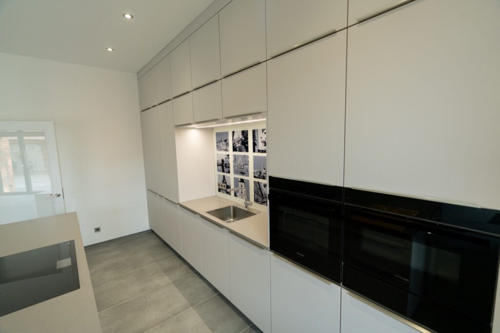 Moderne Küche mit weißen Schränken, Edelstahlspüle, Induktionskochfeld und schwarz-weißen Grafiken.