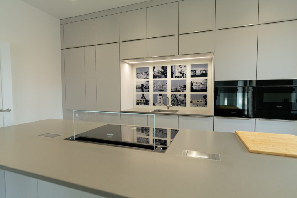 Moderne, minimalistische Küche mit hellem Küchenblock, eingebautem Kochfeld und künstlerischen Fotografien.