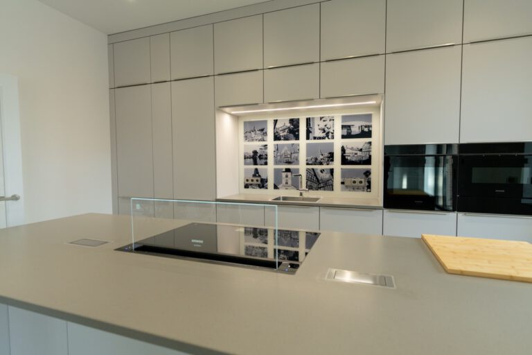 Moderne, minimalistische Küche mit hellem Küchenblock, eingebautem Kochfeld und künstlerischen Fotografien.