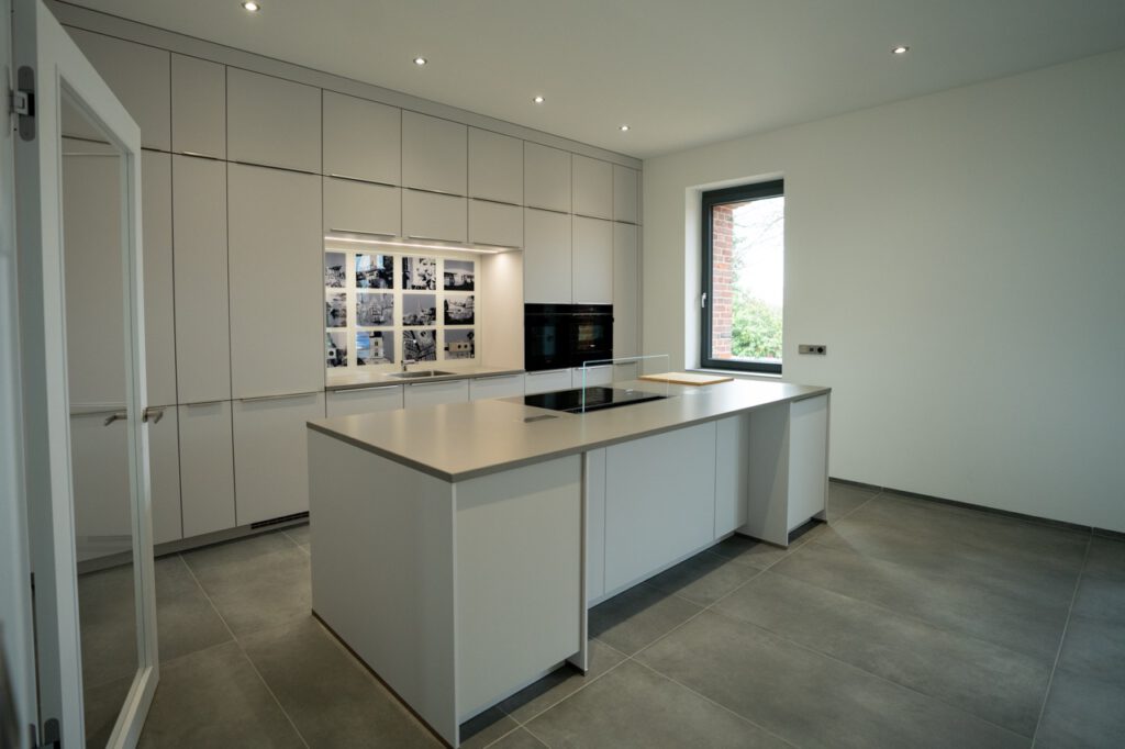 Moderne, minimalistische Küche mit zentraler Insel, weißen Schränken und dekorativer Fotowand.