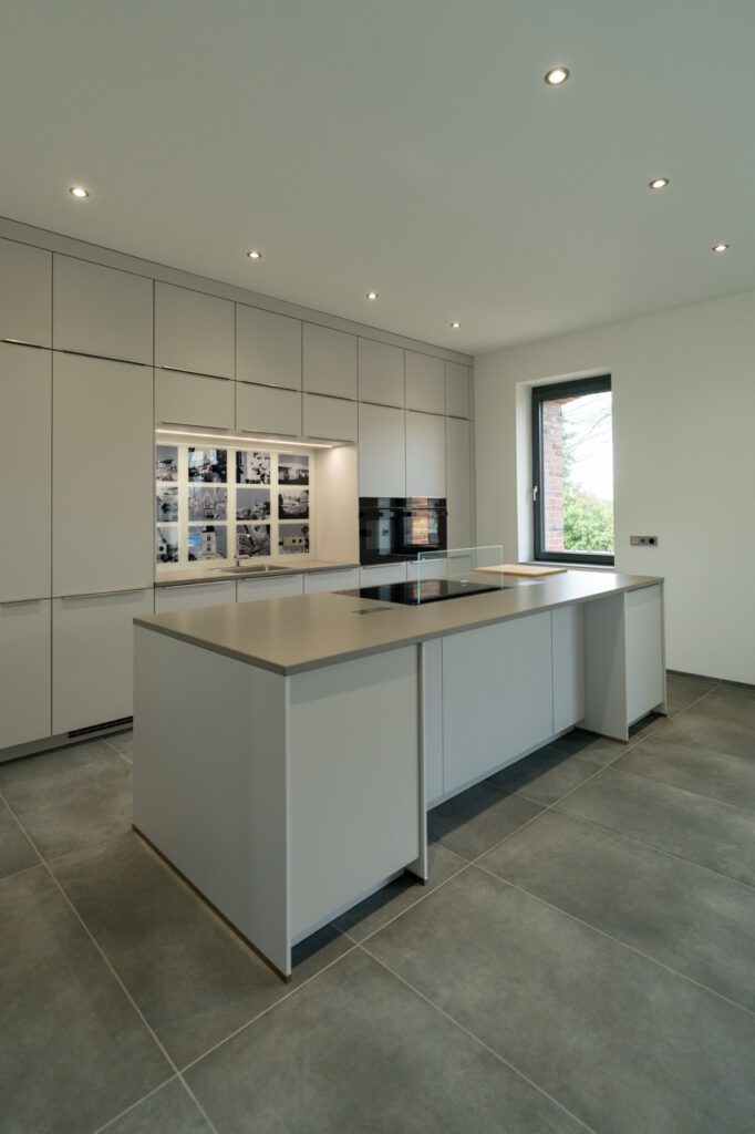 Moderne, minimalistische Küche mit grauer Insel, eingebautem Herd und viel natürlichem Licht.