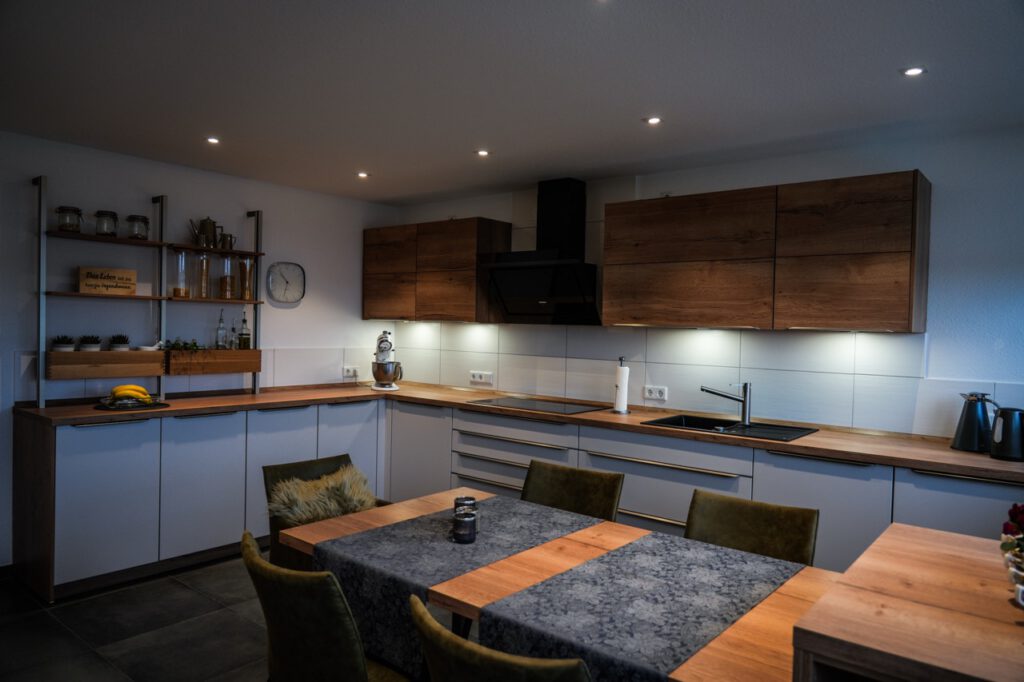Moderne, gut organisierte Küche mit Holz- und weißen Elementen, Tisch und Stühlen in warmen Tönen.