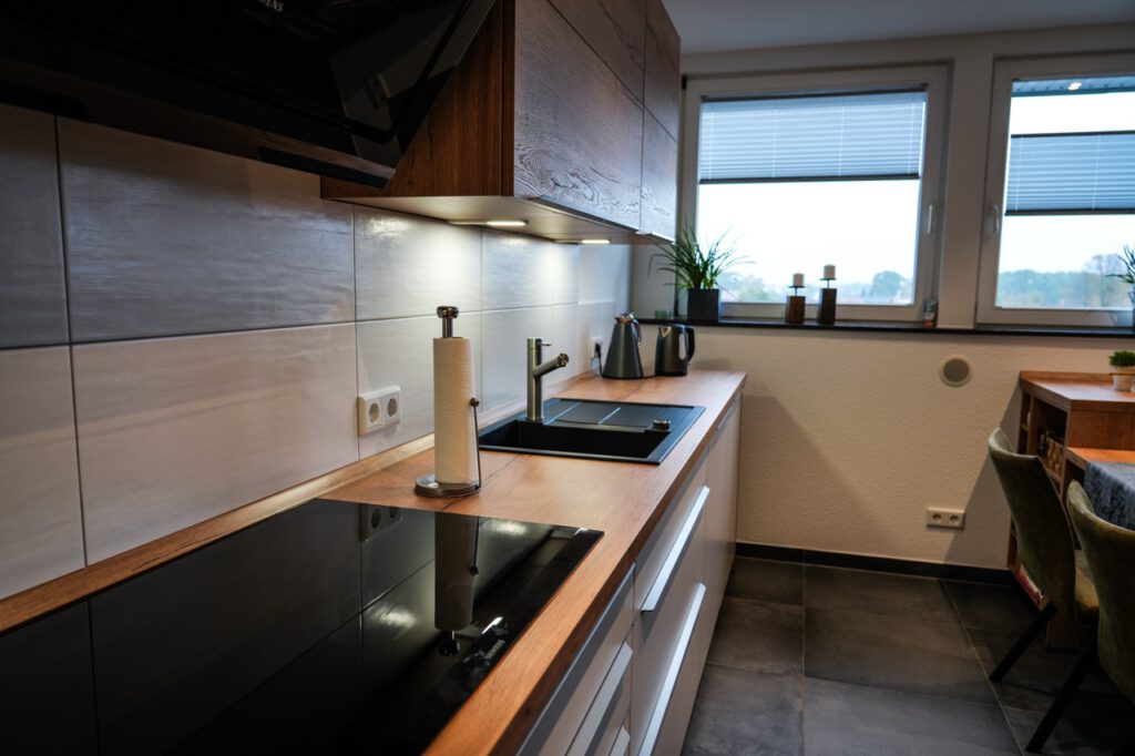 Moderne Küche mit Holzarbeitsplatte, schwarzem Kochfeld, Pflanzen und eleganten Metallakzenten.