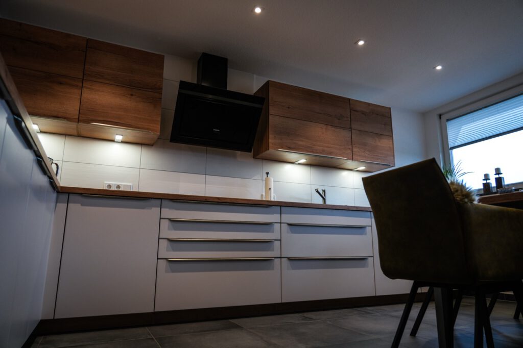 Moderne Küche mit Holzschränken, schwarzer Dunstabzugshaube und warmer Beleuchtung.