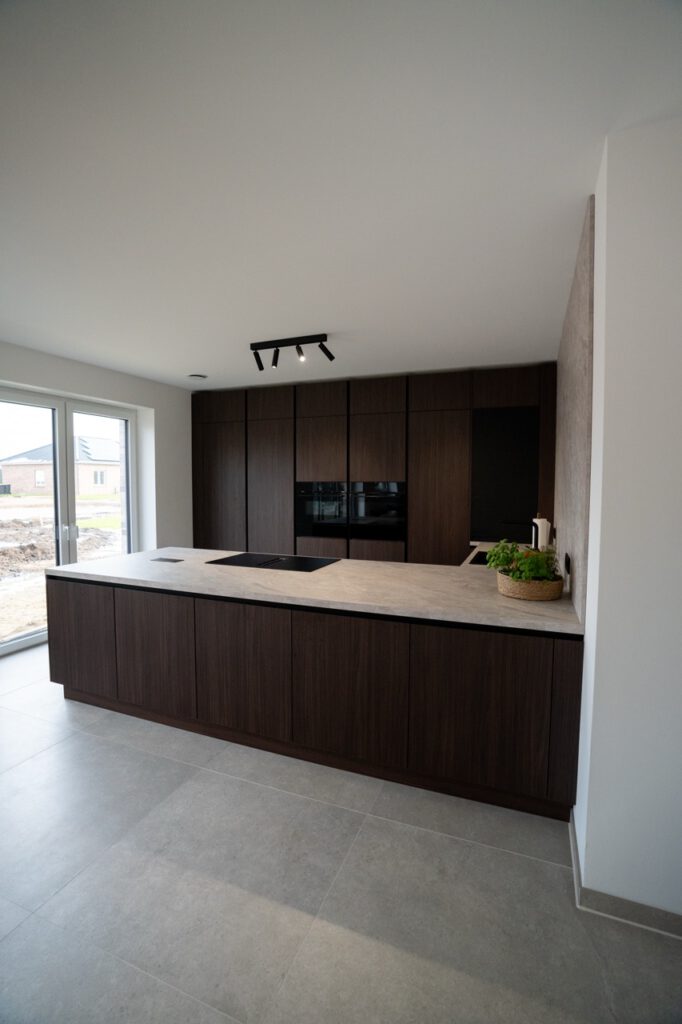 Moderne, aufgeräumte Küche mit dunklen Holzschränken, heller Arbeitsplatte und frischen Kräutern.