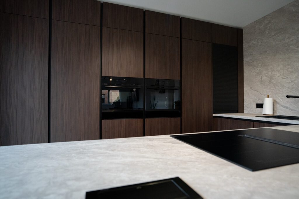Moderne Küche mit dunklen Holzschränken, schwarzen Geräten und heller Stein-Arbeitsplatte.