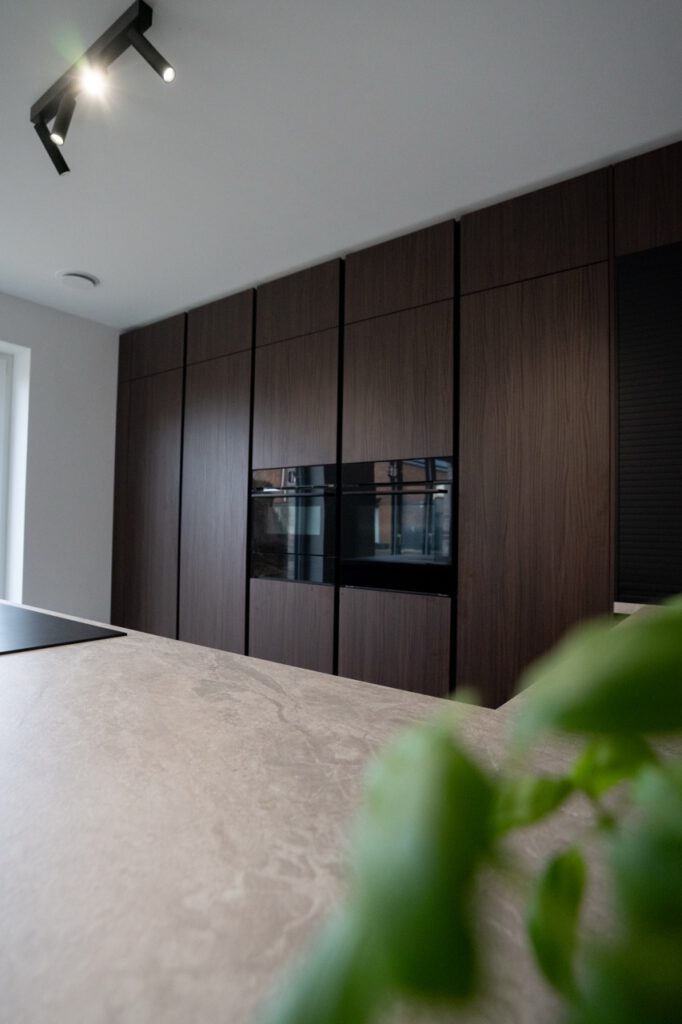Moderne Küche mit dunklen Holzschränken, heller Arbeitsplatte und integrierten Elektrogeräten.