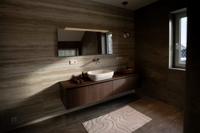 Modernes Badezimmer mit elegantem Design, beleuchtetem Spiegel, ovalem Waschbecken und hölzernem Waschtisch.