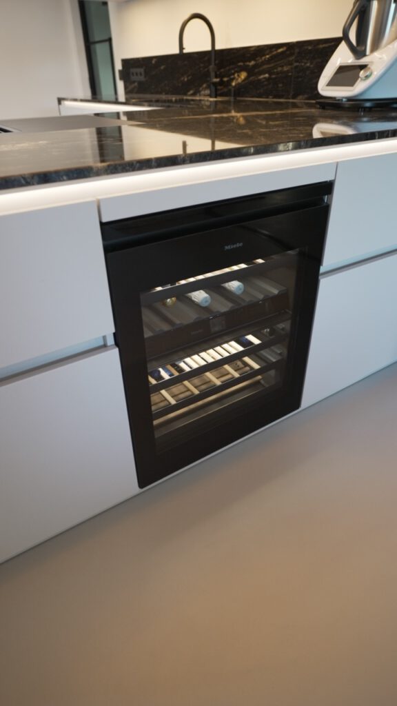 Moderne Küche mit Miele-Weinkühlschrank, schwarzer Marmorarbeitsplatte und Küchenroboter.