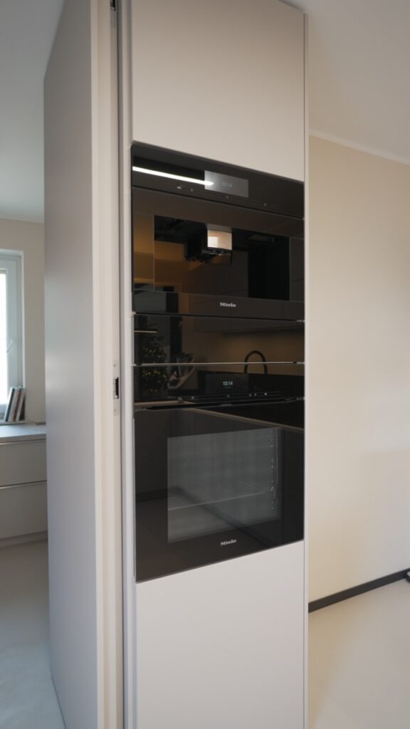 Moderner weißer Küchenschrank mit eingebauten schwarzen Miele-Geräten in heller, minimalistischer Küche.