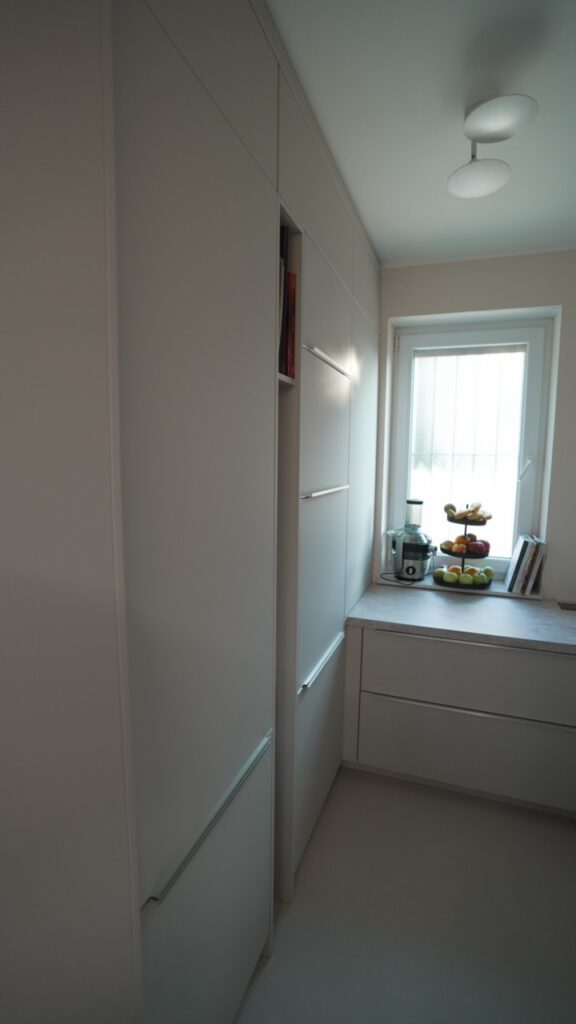 Moderne, minimalistische Küche mit hellen Schränken, Obstkorb und natürlichem Licht durch das Fenster.
