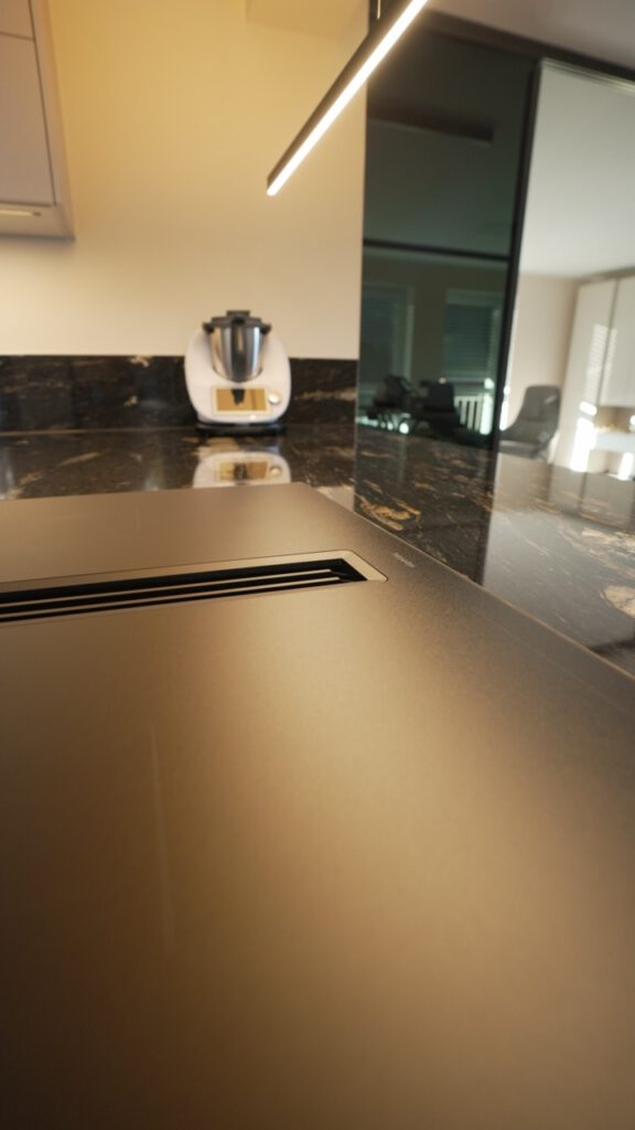 Moderne Küche mit dunkler Granitarbeitsfläche und weißem Küchenkleingerät vor beiger Wand.