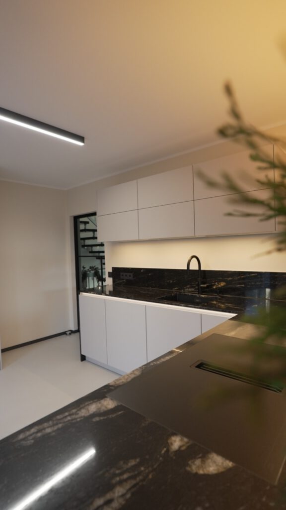 Moderne, minimalistische Küche mit weißen Schränken, dunkler Marmorarbeitsplatte und eleganter Beleuchtung.