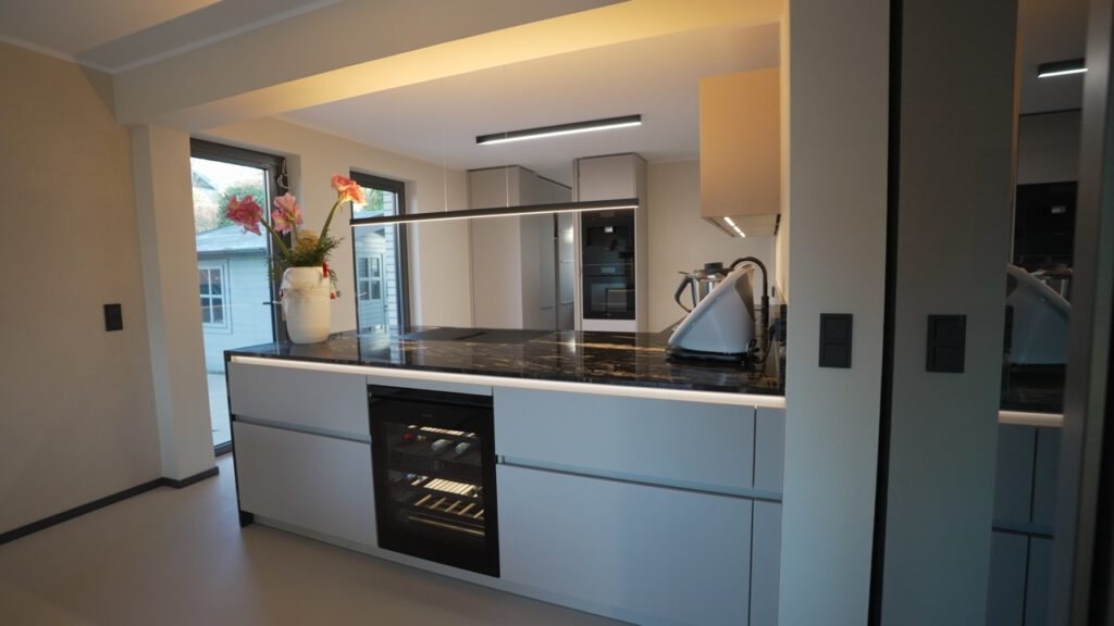 Moderne, aufgeräumte Küche mit schwarzer Marmorinsel, weißem Krug mit roten Blumen und Mixer.