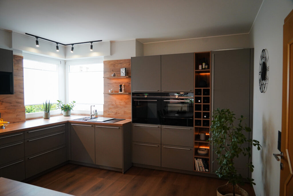 Moderne Küche mit grauen Schränken, Holzarbeitsplatten, Pflanzen und eingebauten Geräten.