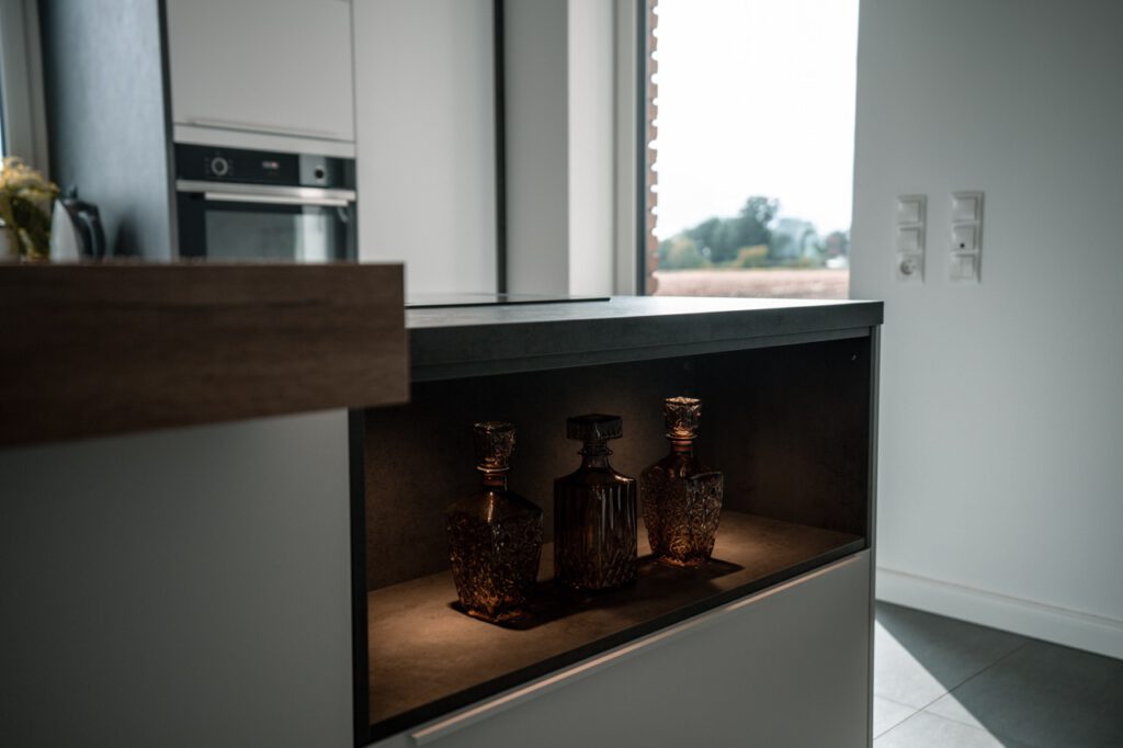 Moderne Küche mit dekorativen Glasflaschen in beleuchtetem Fach, elegantes und gemütliches Ambiente.