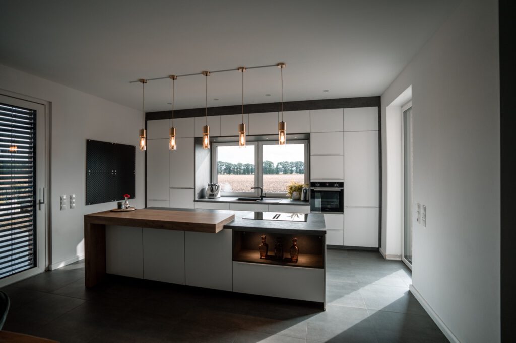 Moderne Küche mit Holzinsel, Pendelleuchten und großem Fenster, das viel Licht hereinlässt.