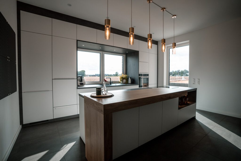 Moderne, aufgeräumte Küche mit Holzarbeitsplatte, warmem Licht und Blick ins Grüne.