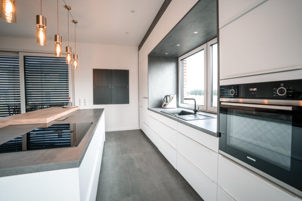 Moderne Küche mit weißen Schränken, grauer Arbeitsplatte, Kücheninsel und warmem Licht.