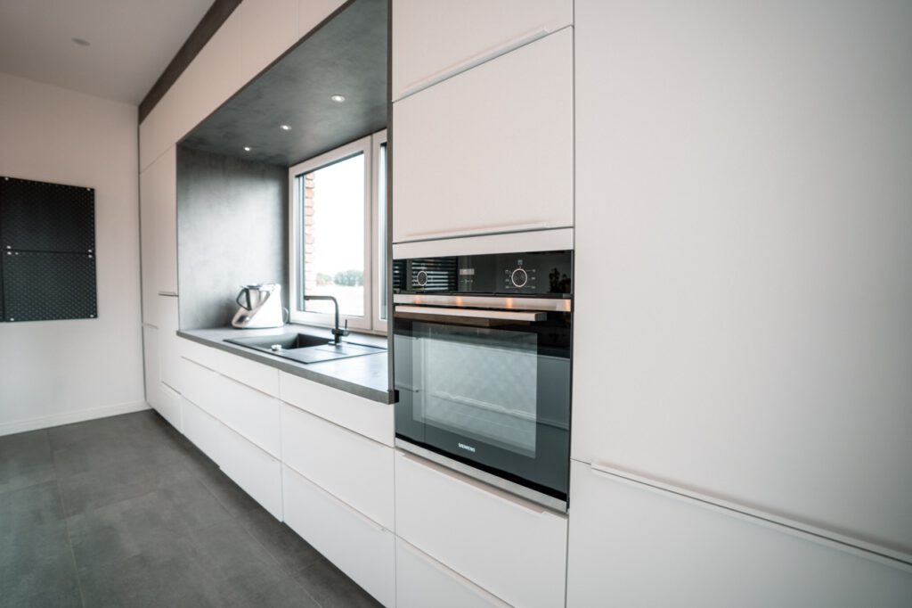 Moderne, minimalistische Küche mit weißen Schränken, schwarzem Backofen und einem Fenster.