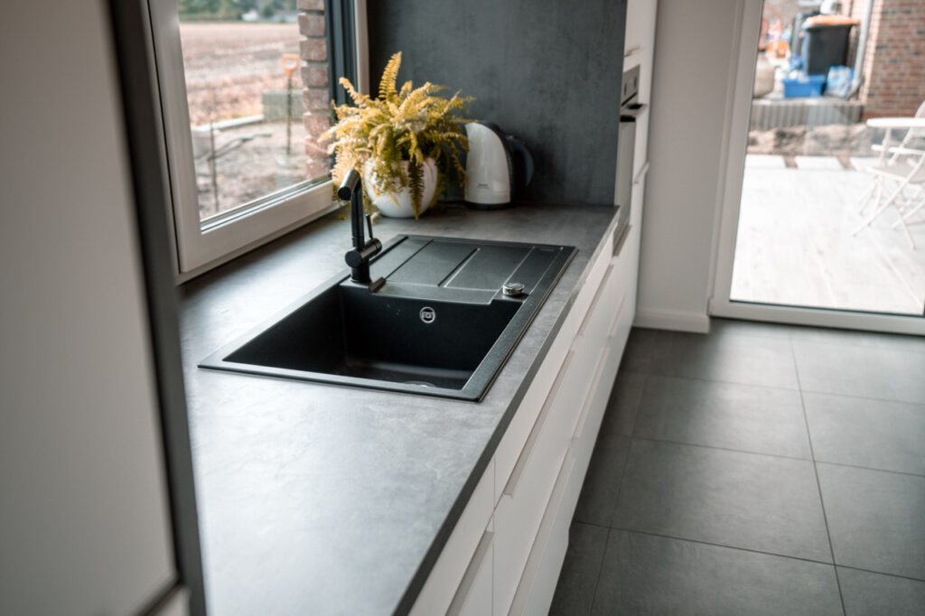 Moderne Küche mit schwarzem Spülbecken, Wasserkocher, Pflanze und grauer Arbeitsplatte.