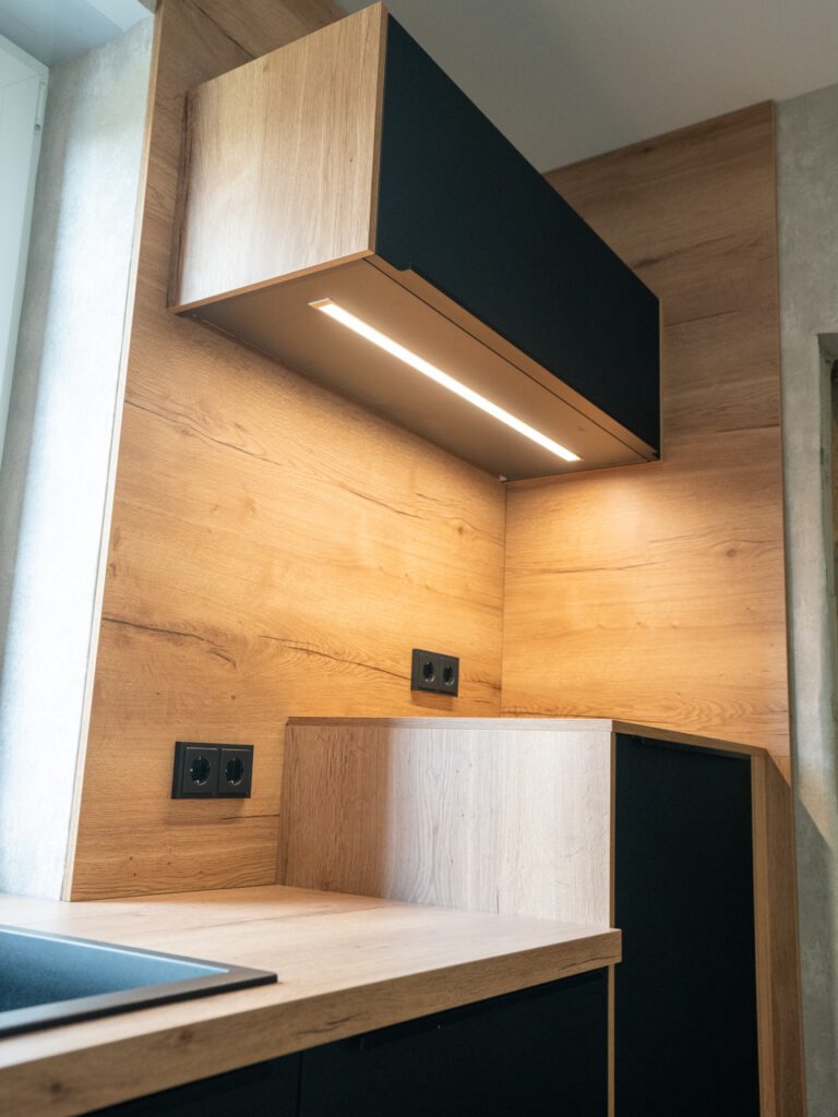 Moderner Küchenbereich mit Holz- und Schwarztönen, integrierter Beleuchtung und minimalistischer Ästhetik.