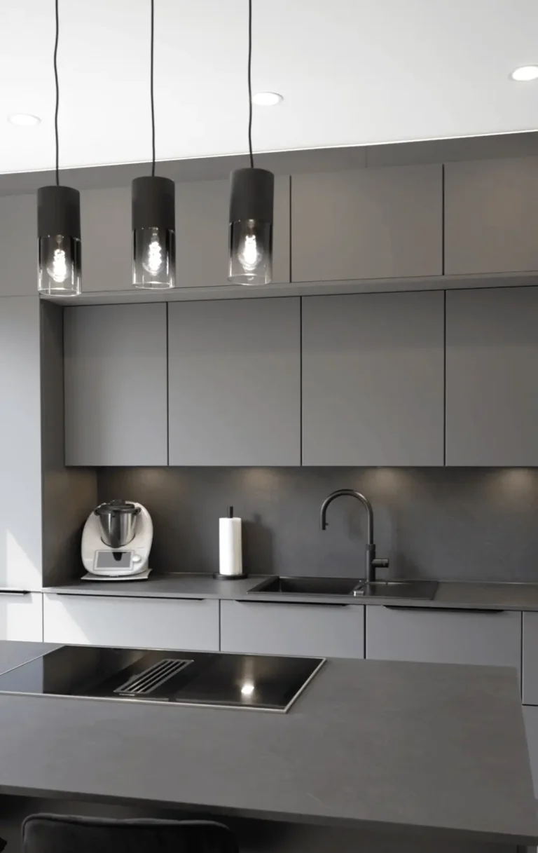 Moderne, minimalistische Küche in Grau mit schwarzen Akzenten, Induktionskochfeld und Hängelampen.