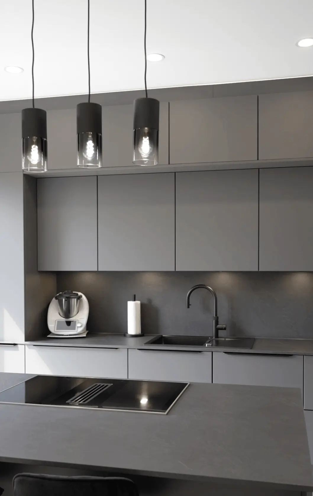 Moderne, minimalistische Küche in Grau mit schwarzen Akzenten, Induktionskochfeld und Hängelampen.