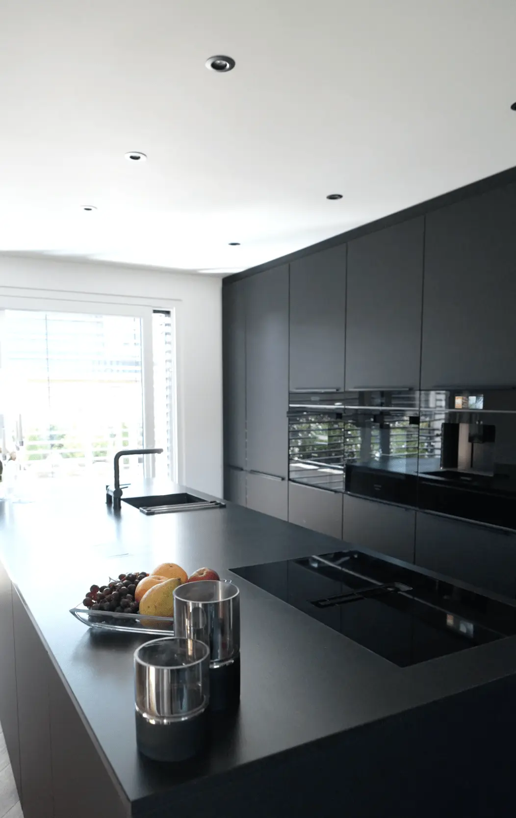 Moderne Küche mit dunkler Insel, glänzenden Schränken, Früchteschale und Kochfeld, elegant beleuchtet.