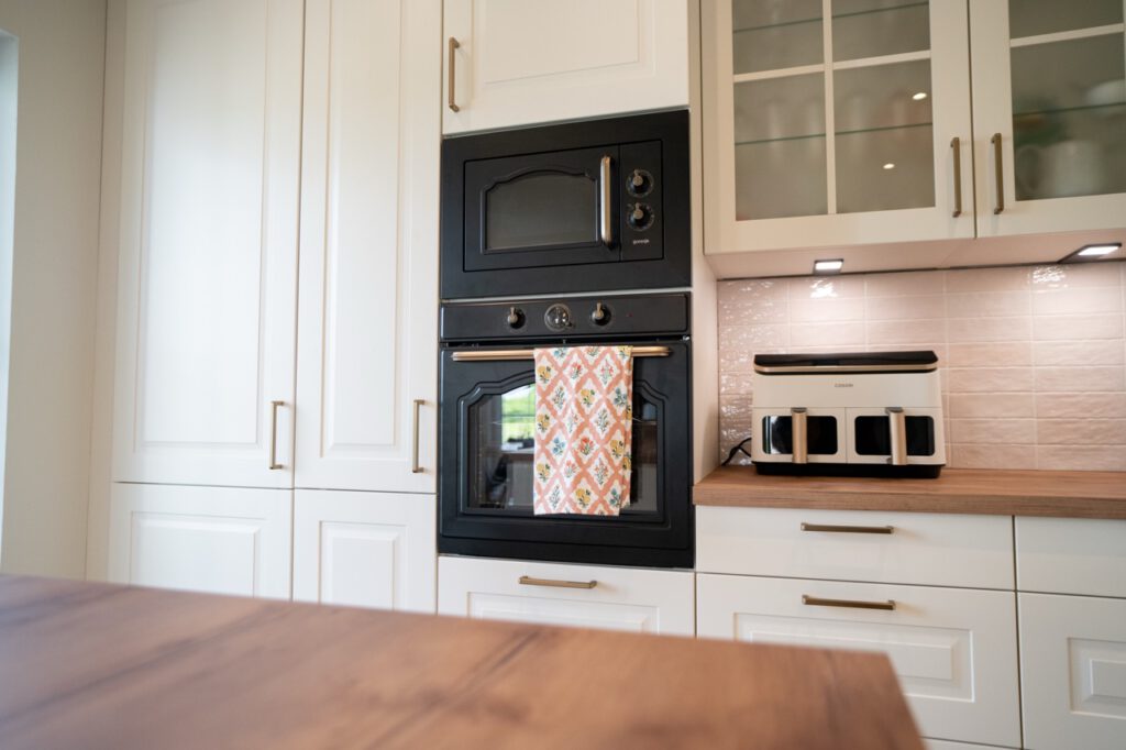 Moderne Küche mit schwarzem Backofen in weißen Schränken, gemustertem Handtuch und Holzarbeitsplatte.