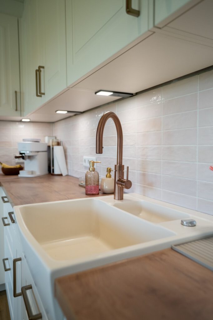 Moderne Küche mit Doppelspüle, bronzenem Wasserhahn, Holzarbeitsplatte und Kaffeemaschine im Hintergrund.